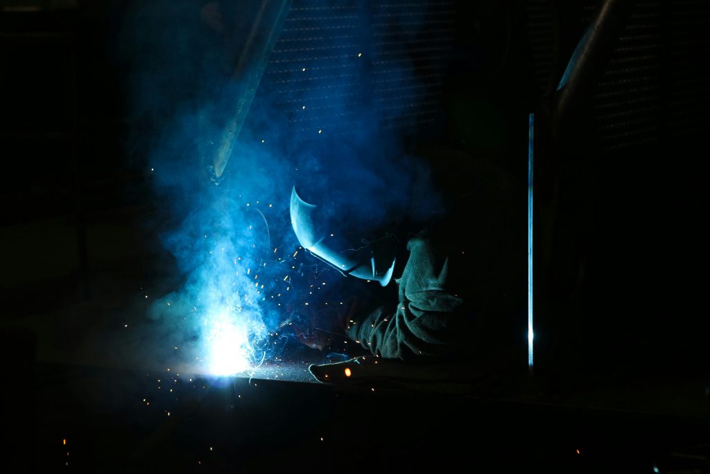 Close-up of a skilled welder working amidst sparks and glowing blue light in a workshop.